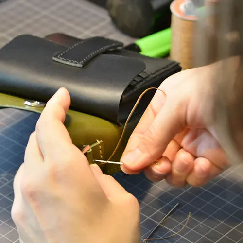 Artisan hand-stitching a custom leather handbag using traditional tools.