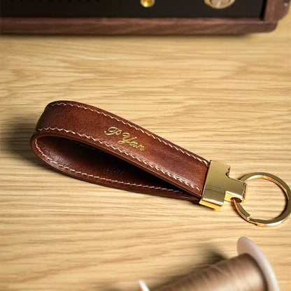 Brown Essen leather key fob with personalized gold foil name in calligraphy style, on a wood surface