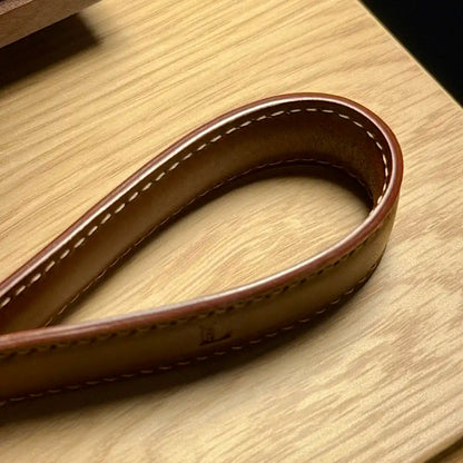 Close-up of brown Essen leather keychain with fascinating stitching & edging highlight, on a wooden surface