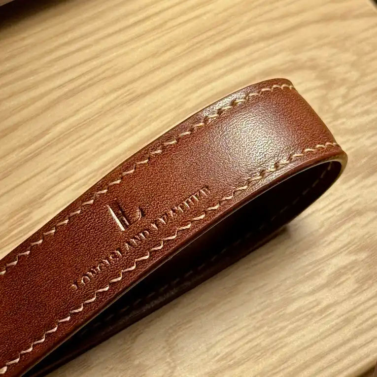 Close-up of a brown Essen leather keychain strap with stitching on a wooden surface, engraved logo of Longisland Leather