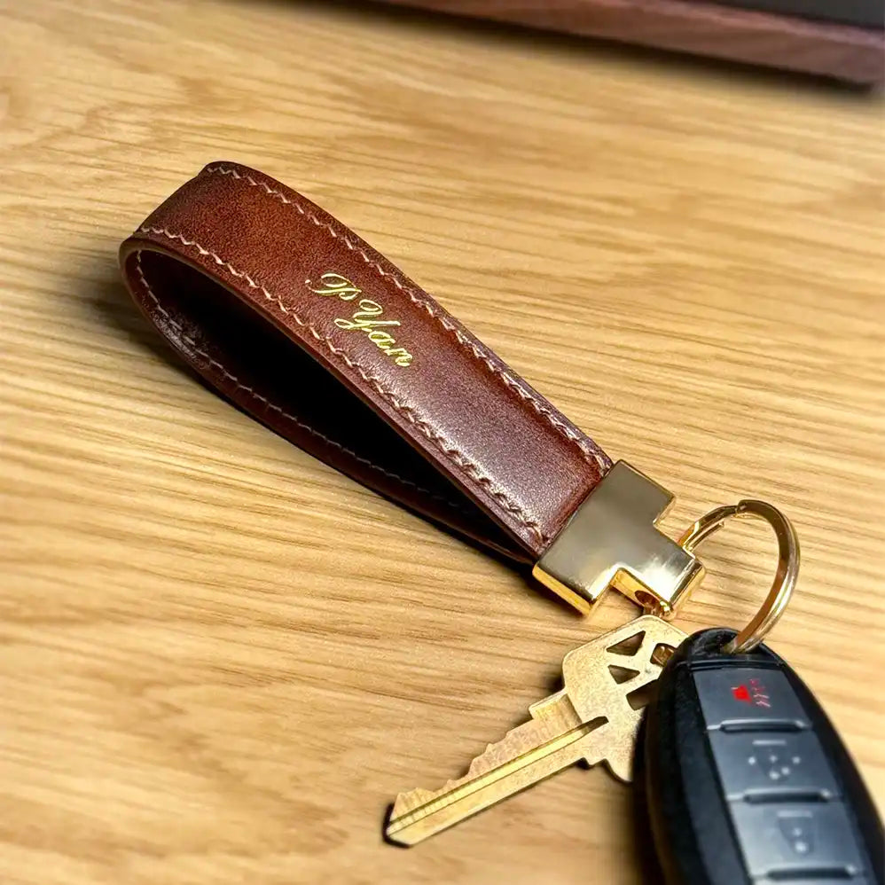 Close-up of brown Essen leather key fob with keys on a wooden surface, with gold foil personalization name