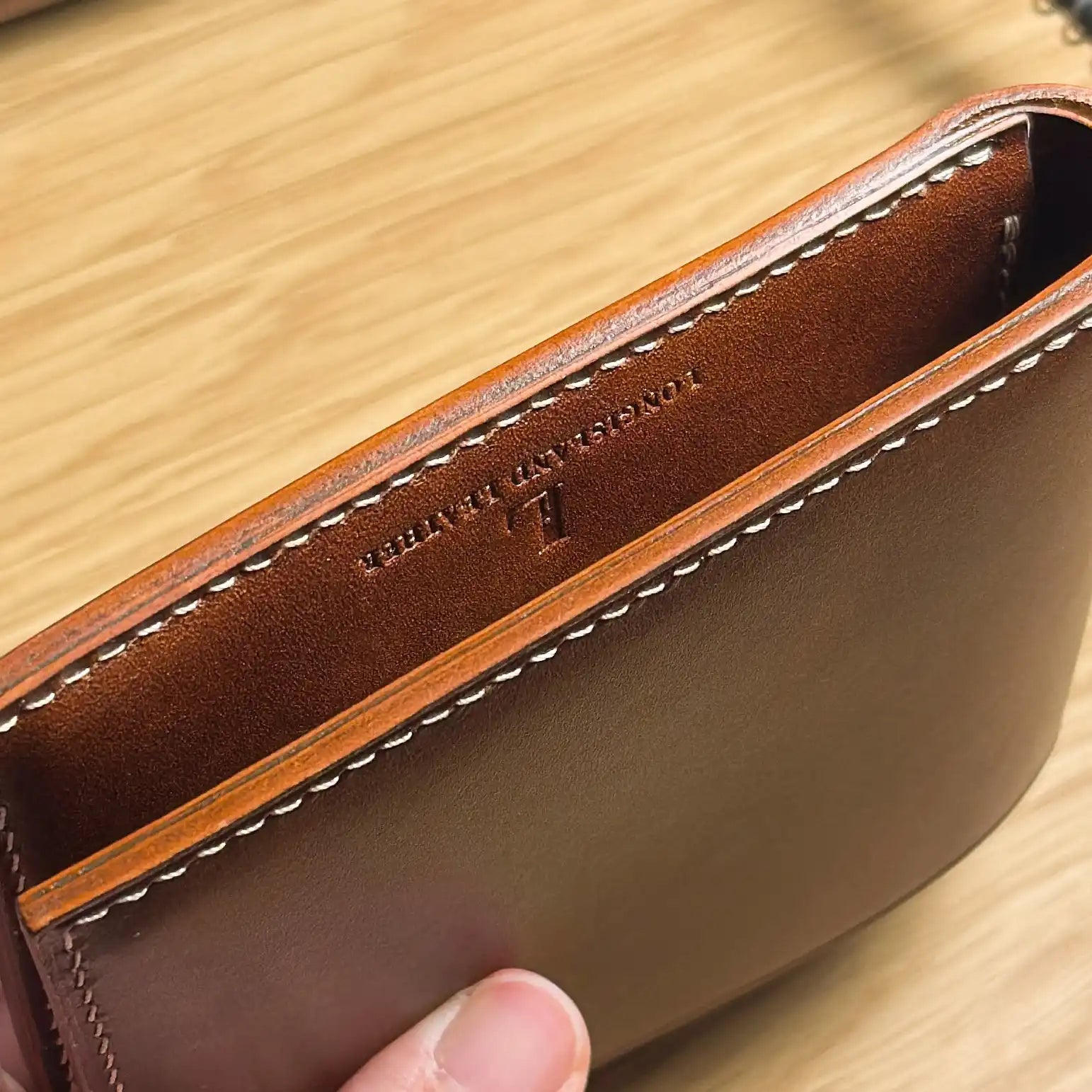Close-up of the burnished edge and precision stitching on the classic bifold leather wallet.