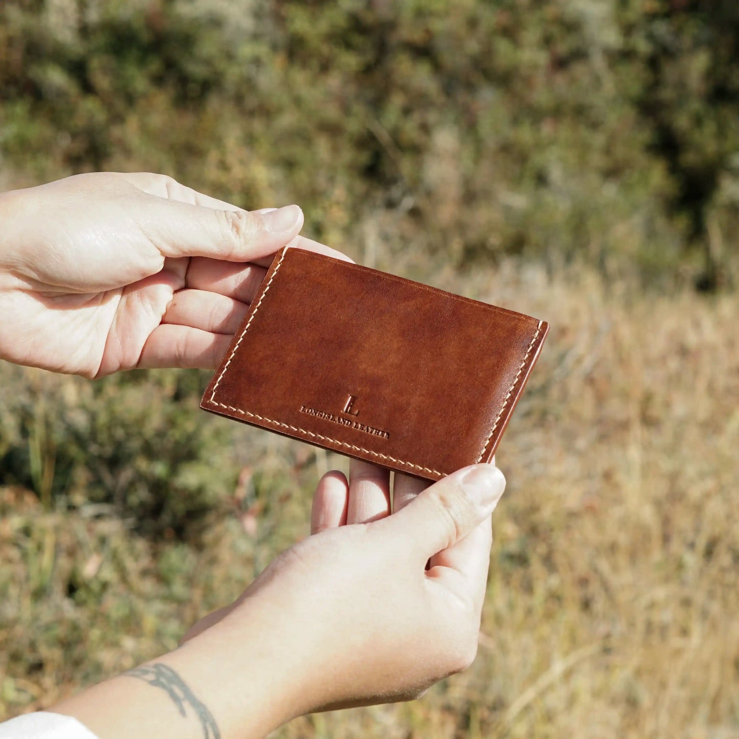 A person holding a handcrafted brown leather card holder outdoors, a perfect personalized gift from Calgary.