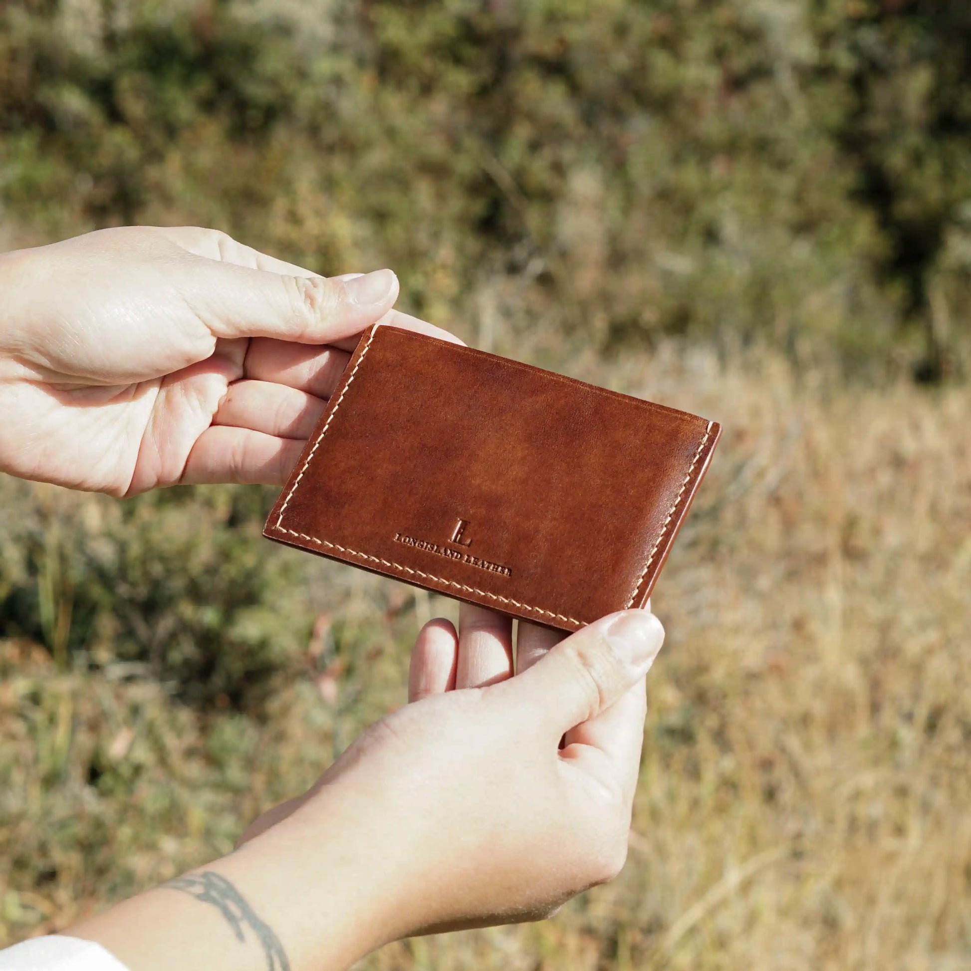 A person holding a handcrafted brown leather card holder outdoors, a perfect personalized gift from Calgary.