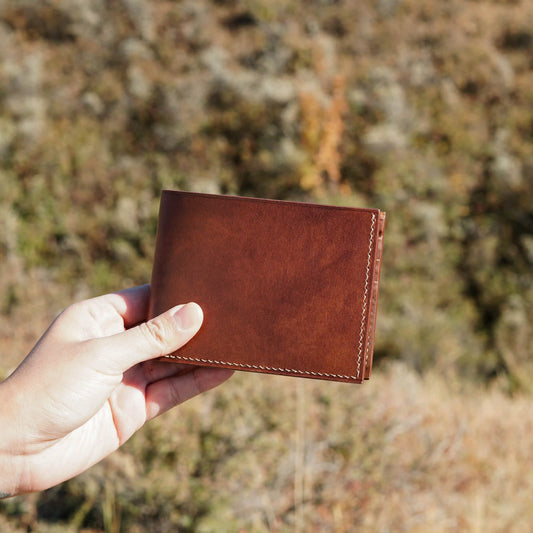 Outdoor shot of artisan holding a handcrafted brown leather bifold wallet, personalized gift from Calgary.