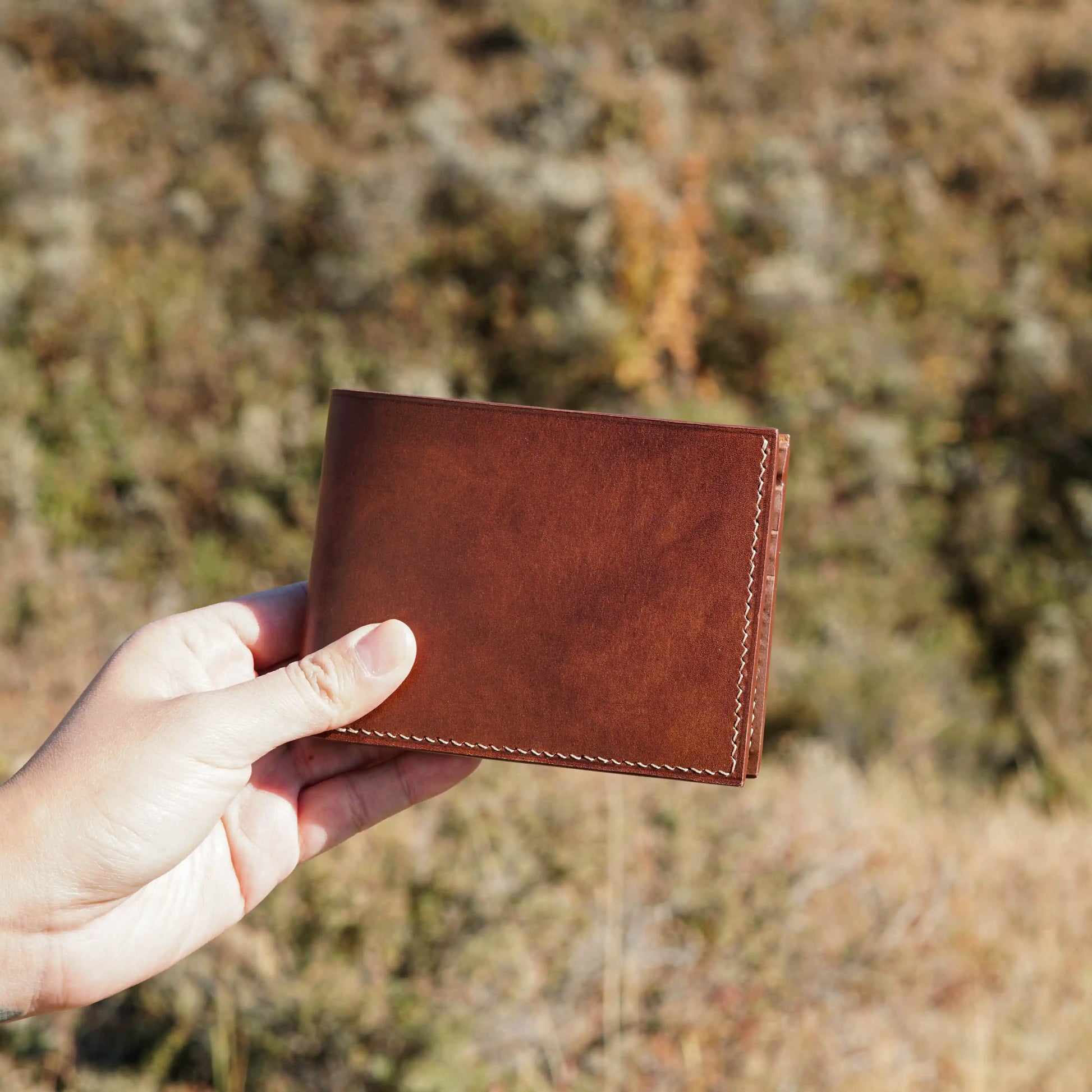 Outdoor shot of artisan holding a handcrafted brown leather bifold wallet, personalized gift from Calgary.