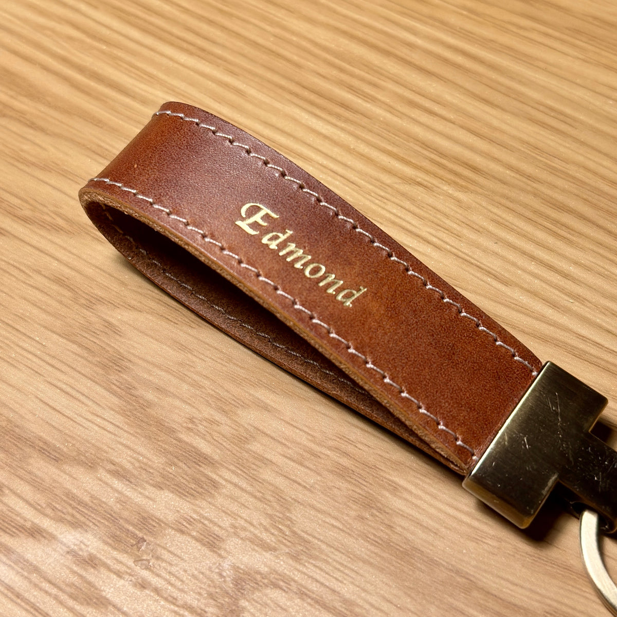 Close-up of gold name stamping and saddle stitching on LOOP brown leather keychain