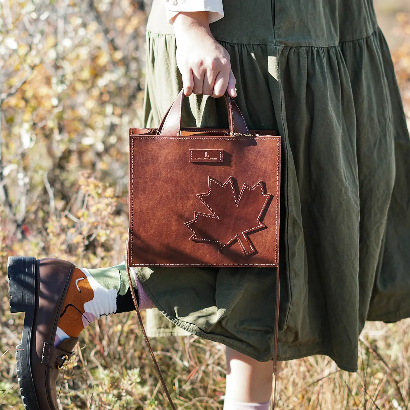 A handcrafted leather handbag featuring a signature maple leaf design, handmade in Calgary, Canada.