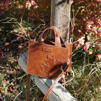 The Maple Heritage leather handbag resting on a rustic wooden post, showcasing its rich brown patina.