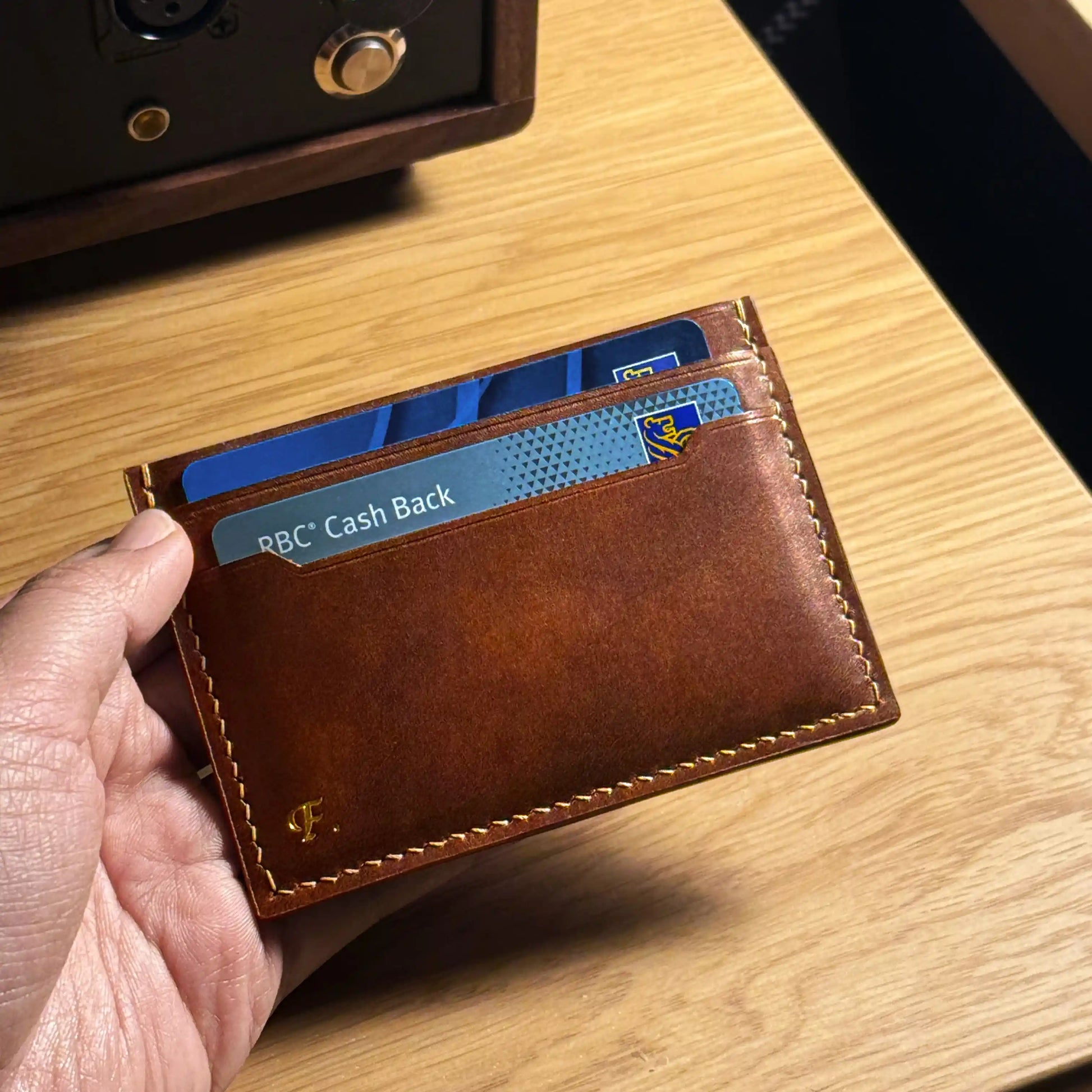 Handheld view of a personalized leather wallet featuring custom gold foil initials on the back.