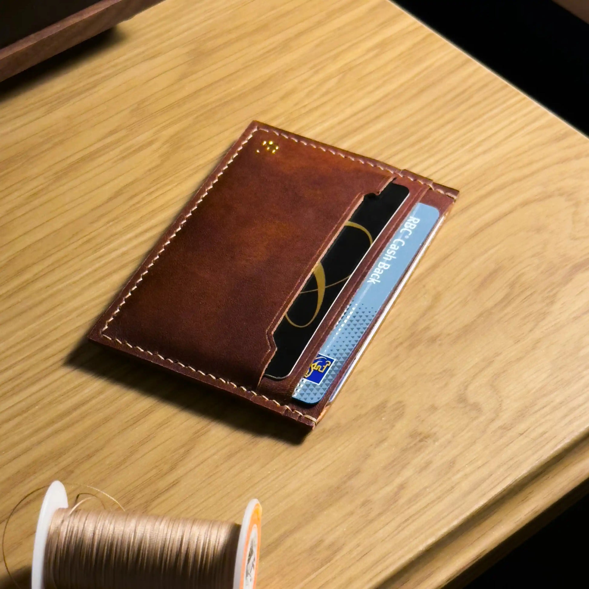 Minimalist leather card holder placed next to sewing thread, highlighting traditional crafting materials.