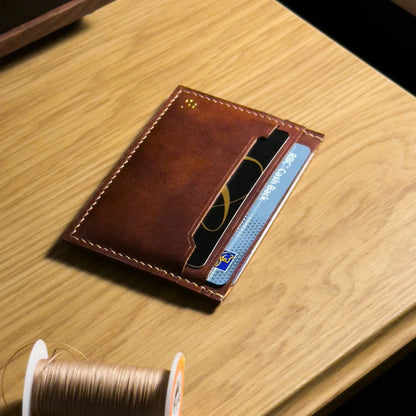 Minimalist leather card holder placed next to sewing thread, highlighting traditional crafting materials.