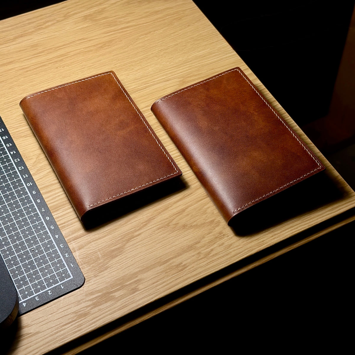 Two closed brown Italian leather passport covers with contrasting saddle stitching